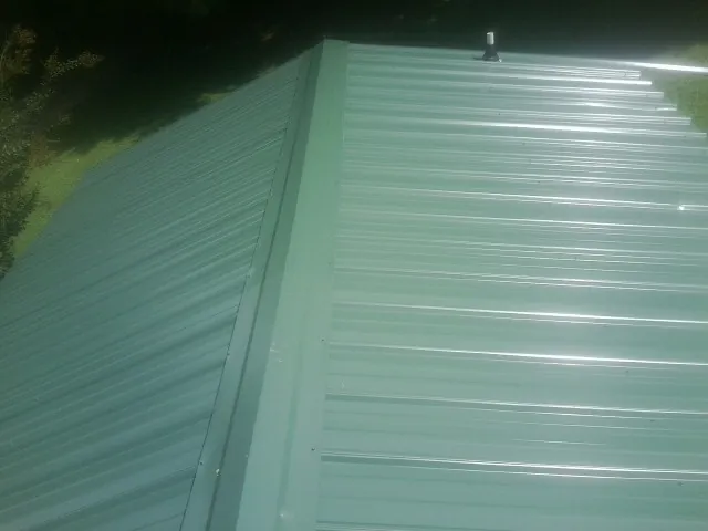 New green metal panels meeting at the ridge of a roof — Flat Roof Repair work by our crew in Plummer