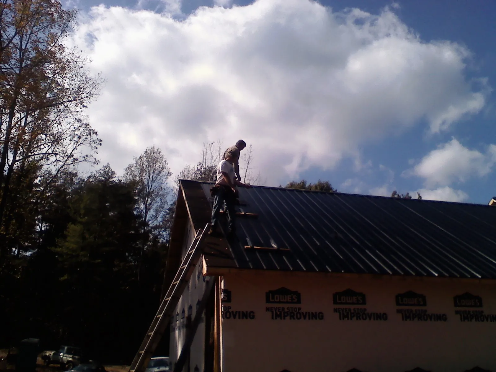 Roofer fastening dark metal panels high against a cloudy sky, from a Roof Inspection job in Plummer